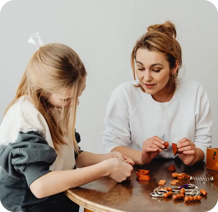 Een vrouw en een meisje zitten aan een ronde houten tafel en leggen samen puzzels van houten stukjes